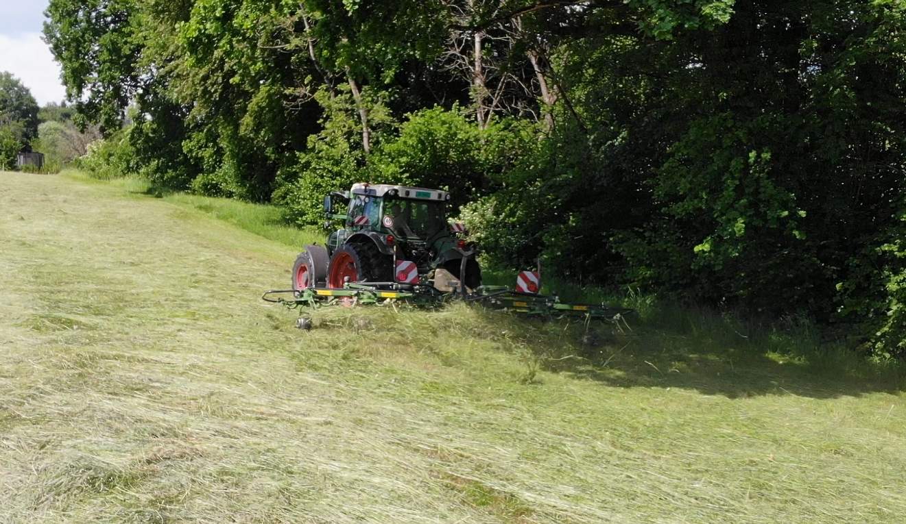 Traktor bei der Heuernte auf einer Wiese am Waldrand